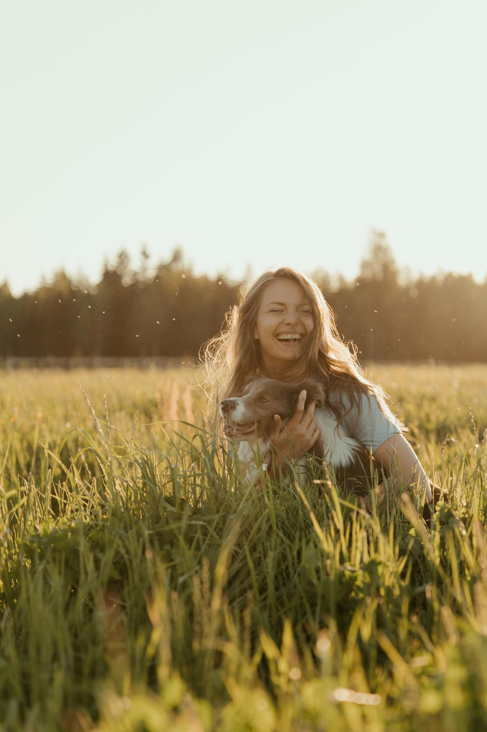 Smiling woman with her pet dog in a sunlit meadow during summer.